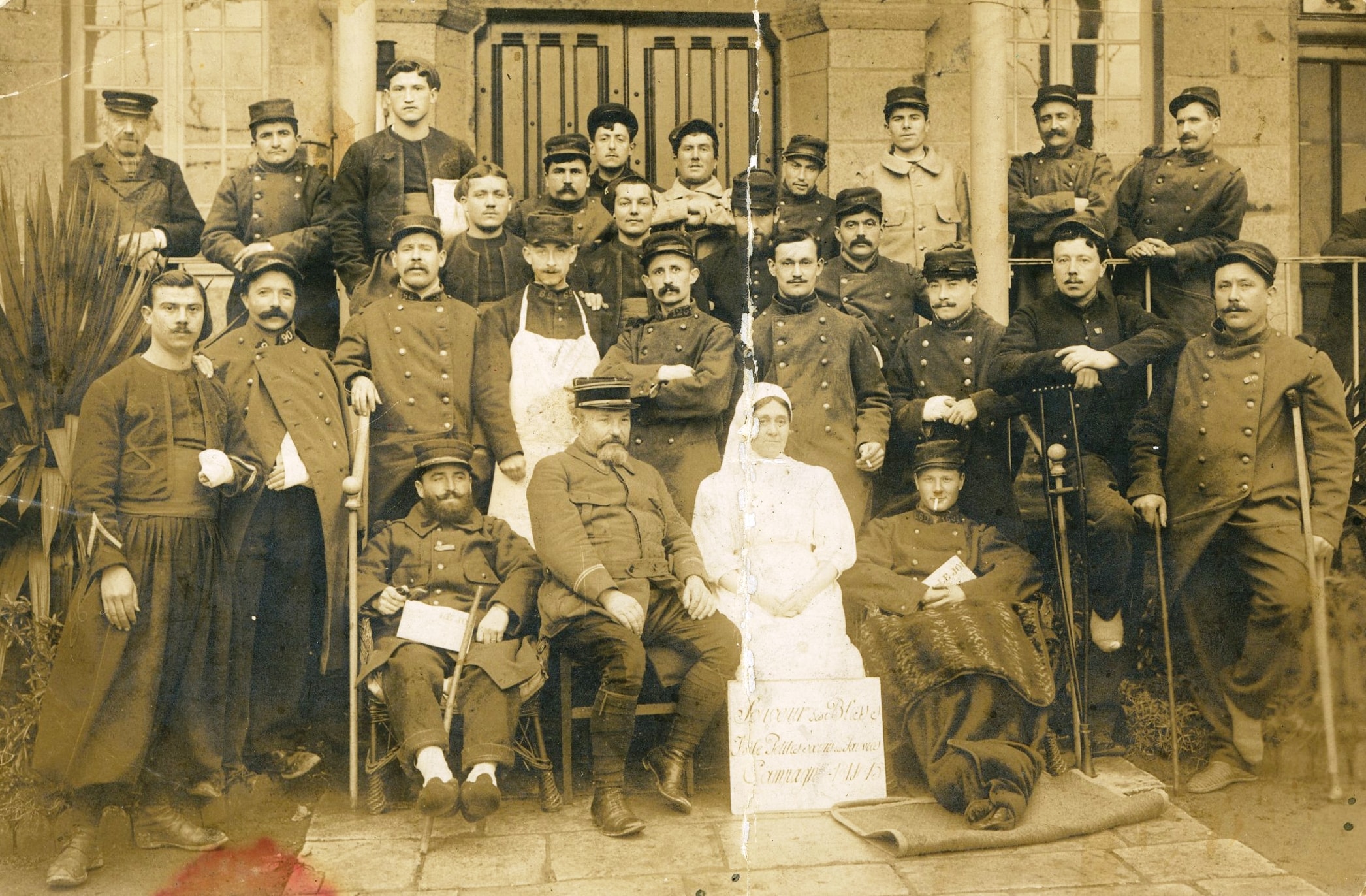 Groupe de soldats blessés et d'infirmières à l'hôpital de Flers (Orne). Photographie carte postale de Fernand Devillers, 29e RA, de Pierrefitte-sur-Seine (Seine-Saint-Denis). 26 janvier 1915. Archives nationales, 700AP/15/PI_02